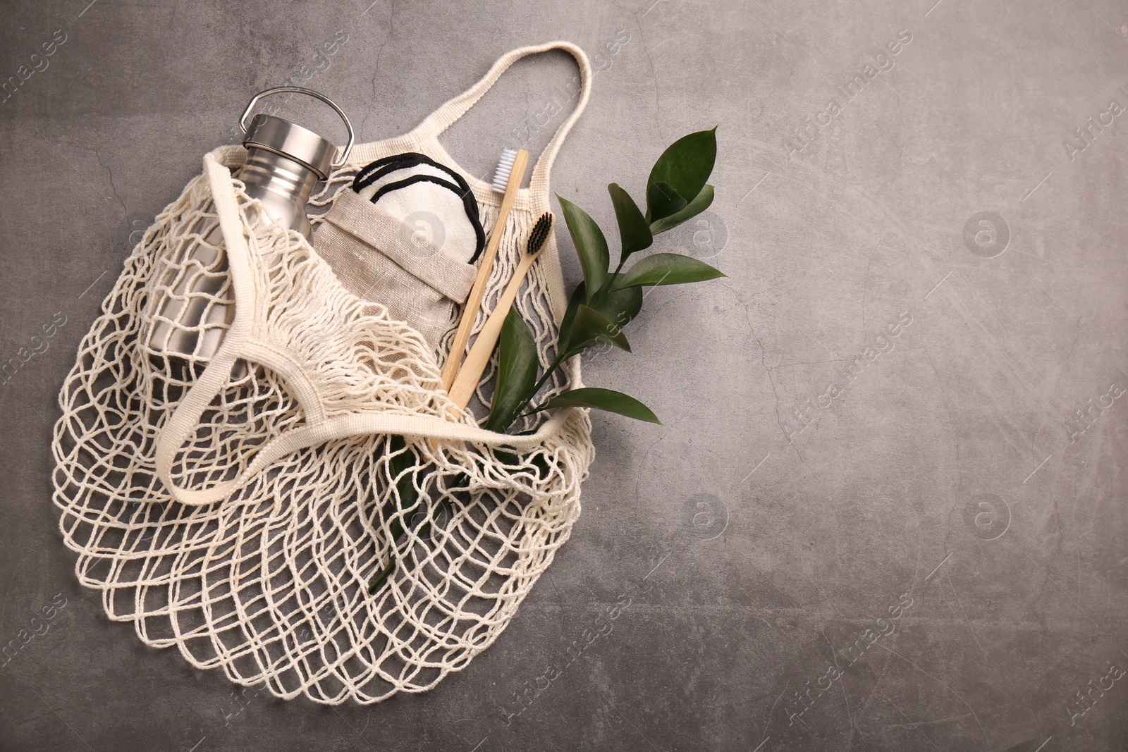 Photo of Fishnet bag with different items and green twig on grey table, top view and space for text. Conscious consumption