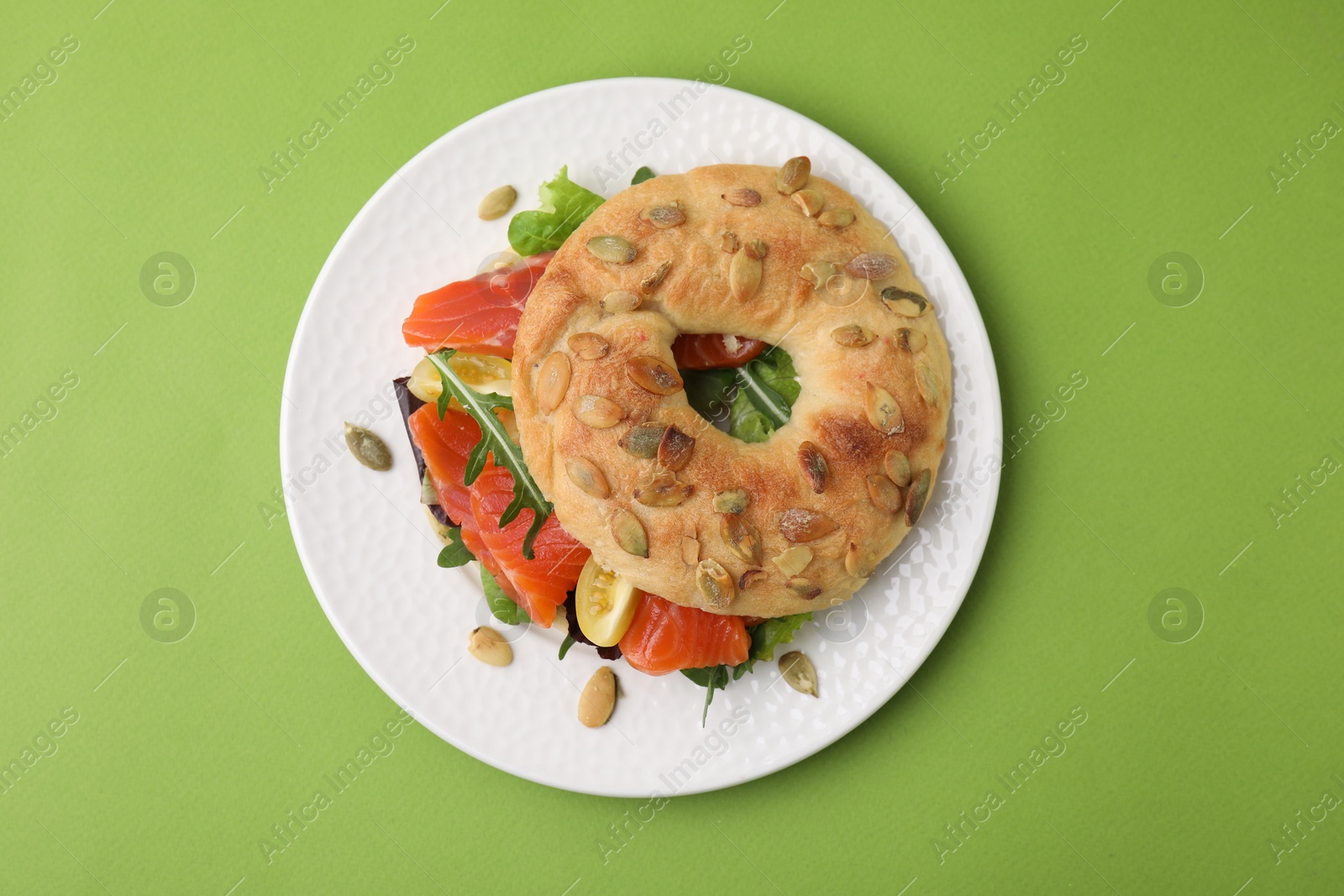 Photo of Tasty bagel with salmon and tomatoes on light green background, top view