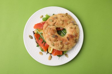 Photo of Tasty bagel with salmon and tomatoes on light green background, top view