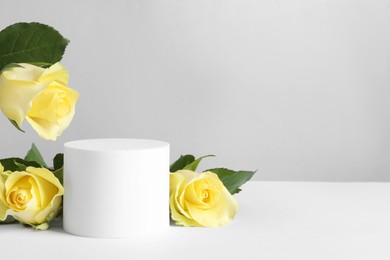 Photo of Beautiful presentation for product. Round podium and yellow roses on white table against light grey background, space for text