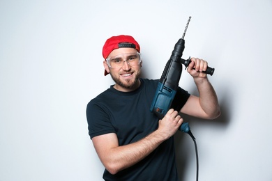 Young working man with rotary hammer on light background