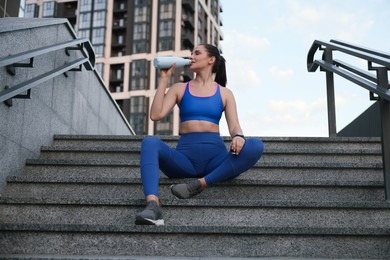 Photo of Beautiful woman in stylish sportswear drinking water on stairs outdoors
