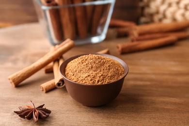 Photo of Bowl with aromatic cinnamon powder and sticks on wooden table