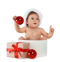 Photo of Cute little baby wearing Santa hat sitting in box with Christmas gift on white background