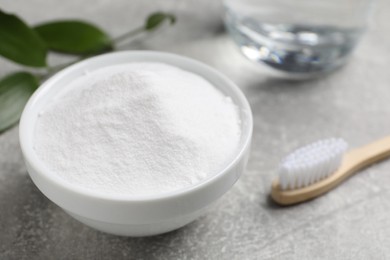 Bamboo toothbrush, green leaf and bowl of baking soda on grey table, closeup. Space for text