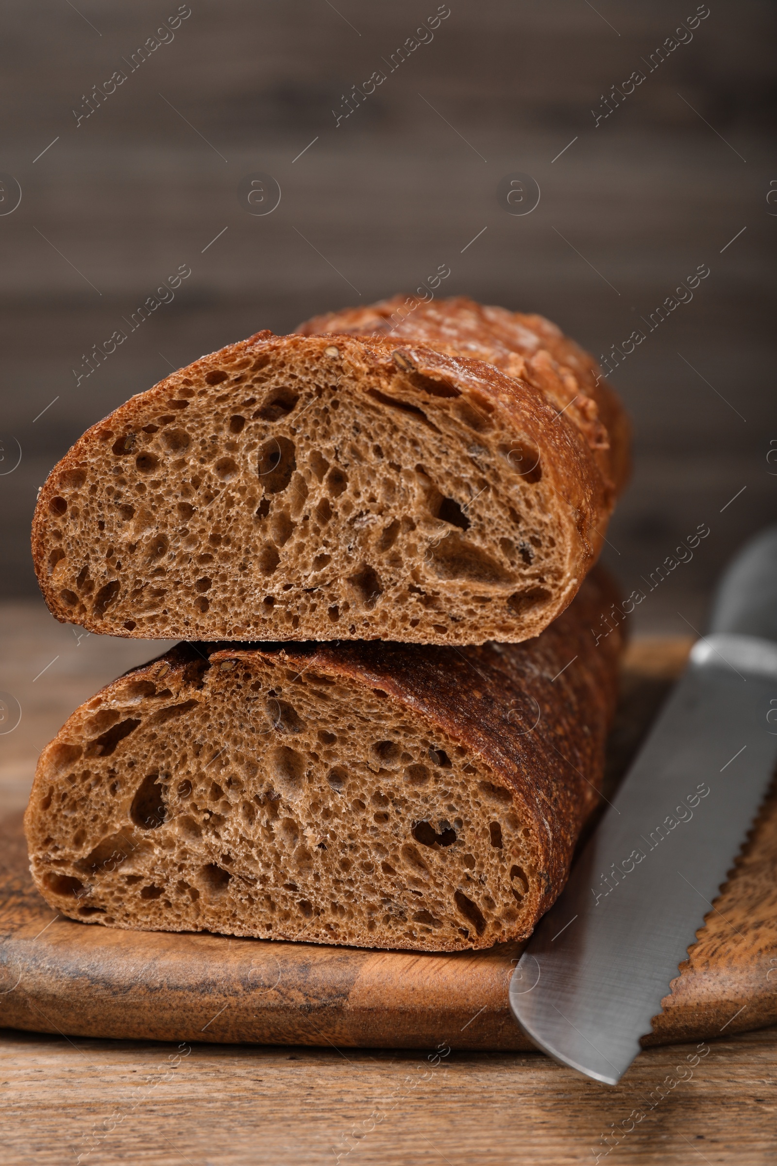 Photo of Cut rye baguette with knife on wooden table, closeup