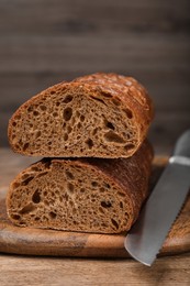 Photo of Cut rye baguette with knife on wooden table, closeup