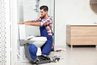 Professional plumber working with toilet bowl in bathroom