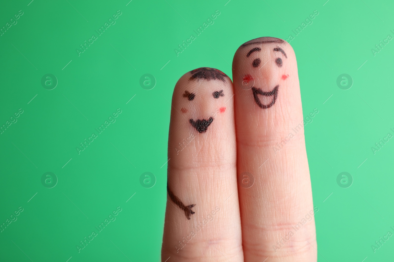 Photo of Two fingers with drawings of happy faces on green background. Spending time together