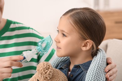 Mother helping her sick daughter with nebulizer inhalation at home