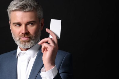 Handsome businessman holding blank business card on black background. Space for text