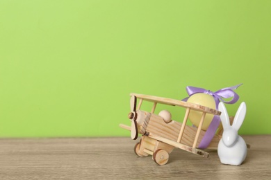 Wooden airplane with dyed egg and cute Easter bunny on table against color background, space for text