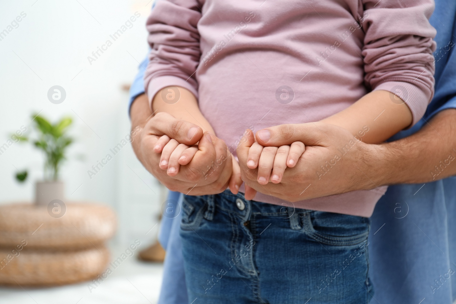 Photo of Father holding hands with his child indoors, closeup. Happy family