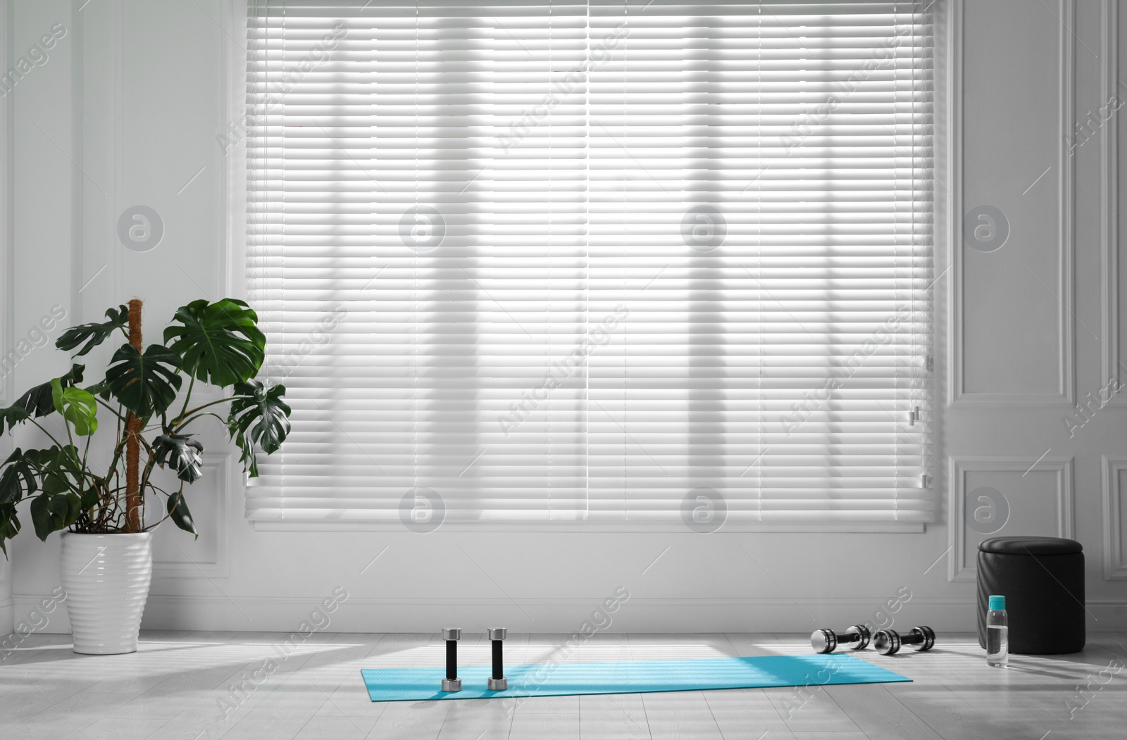 Photo of Exercise mat, dumbbells and bottle of water near window in spacious room