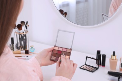 Woman with eyeshadow palette and brush at dressing table, closeup