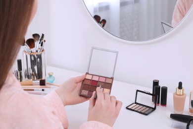 Photo of Woman with eyeshadow palette and brush at dressing table, closeup