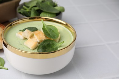 Delicious spinach cream soup with croutons in bowl on white tiled table. Space for text