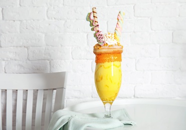 Glass of tasty milk shake with sweets on table near brick wall