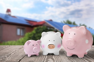 Image of Piggy banks on wooden surface and blurred view of beautiful house. Mortgage concept