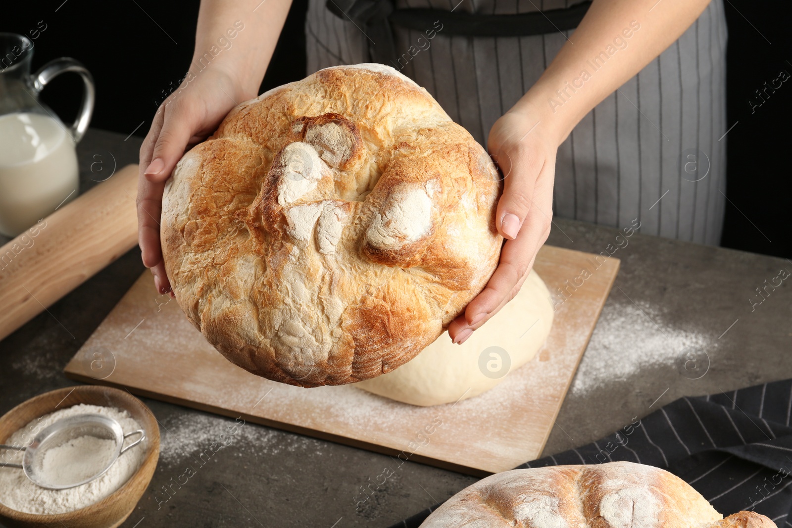 Photo of Female baker holding loaf of bread over kitchen table, closeup