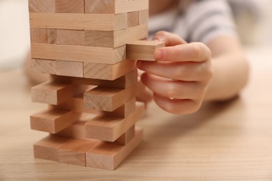 Photo of Child playing Jenga at wooden table indoors, closeup