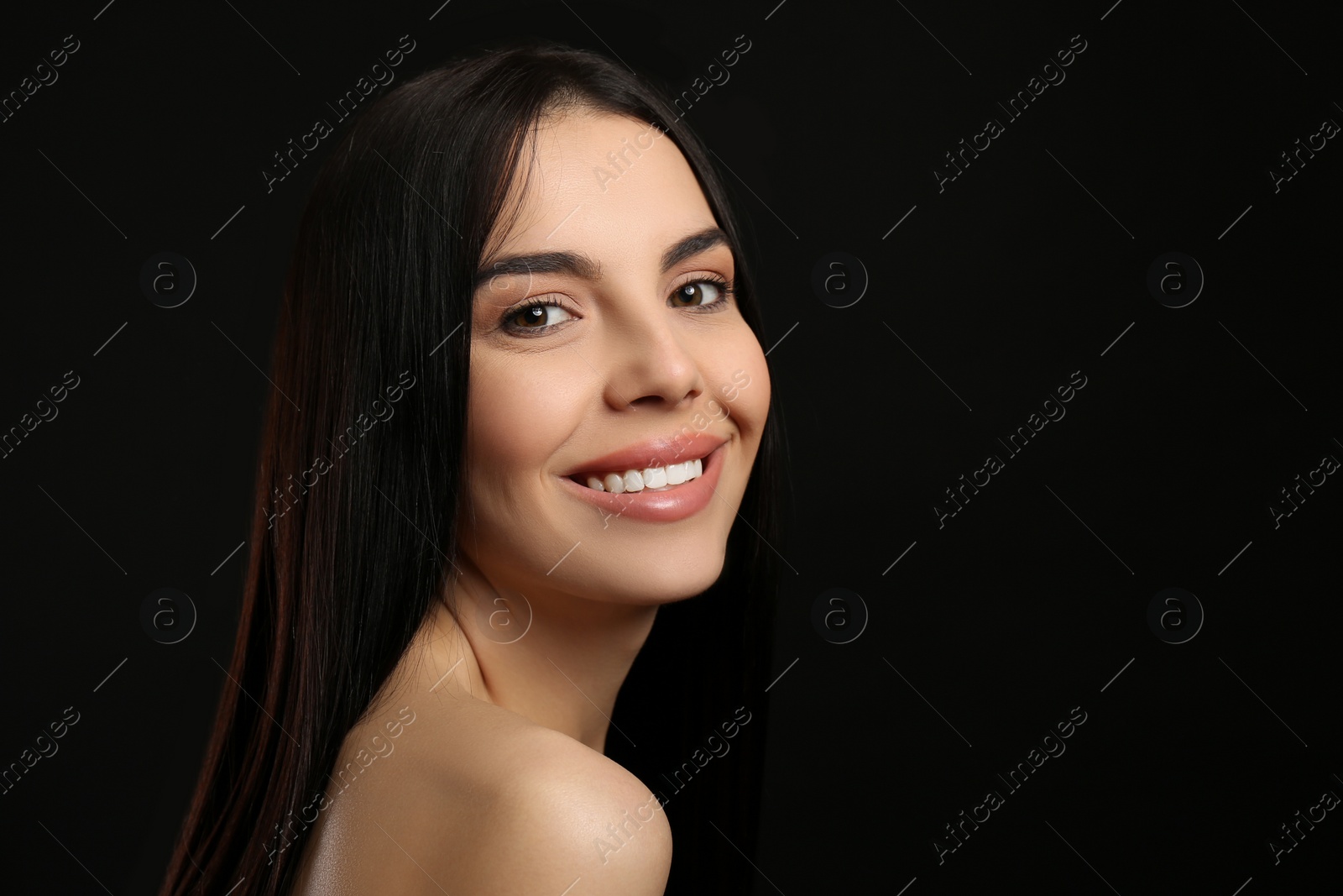 Photo of Portrait of happy young woman with beautiful black hair and charming smile on dark background, space for text