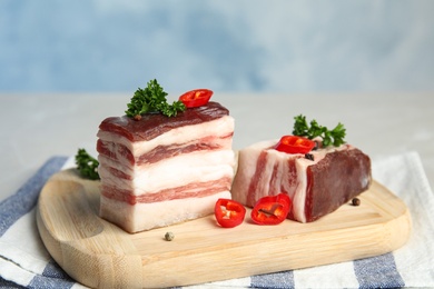 Photo of Board with bacon, parsley and pepper on table against blue background