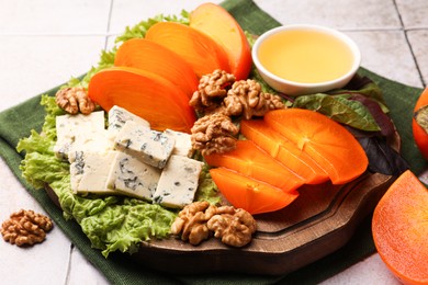 Photo of Delicious persimmon, blue cheese, nuts and honey served on tiled surface, closeup