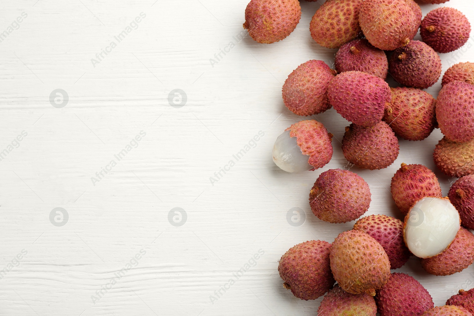 Photo of Fresh ripe lychees on white wooden table, flat lay. Space for text