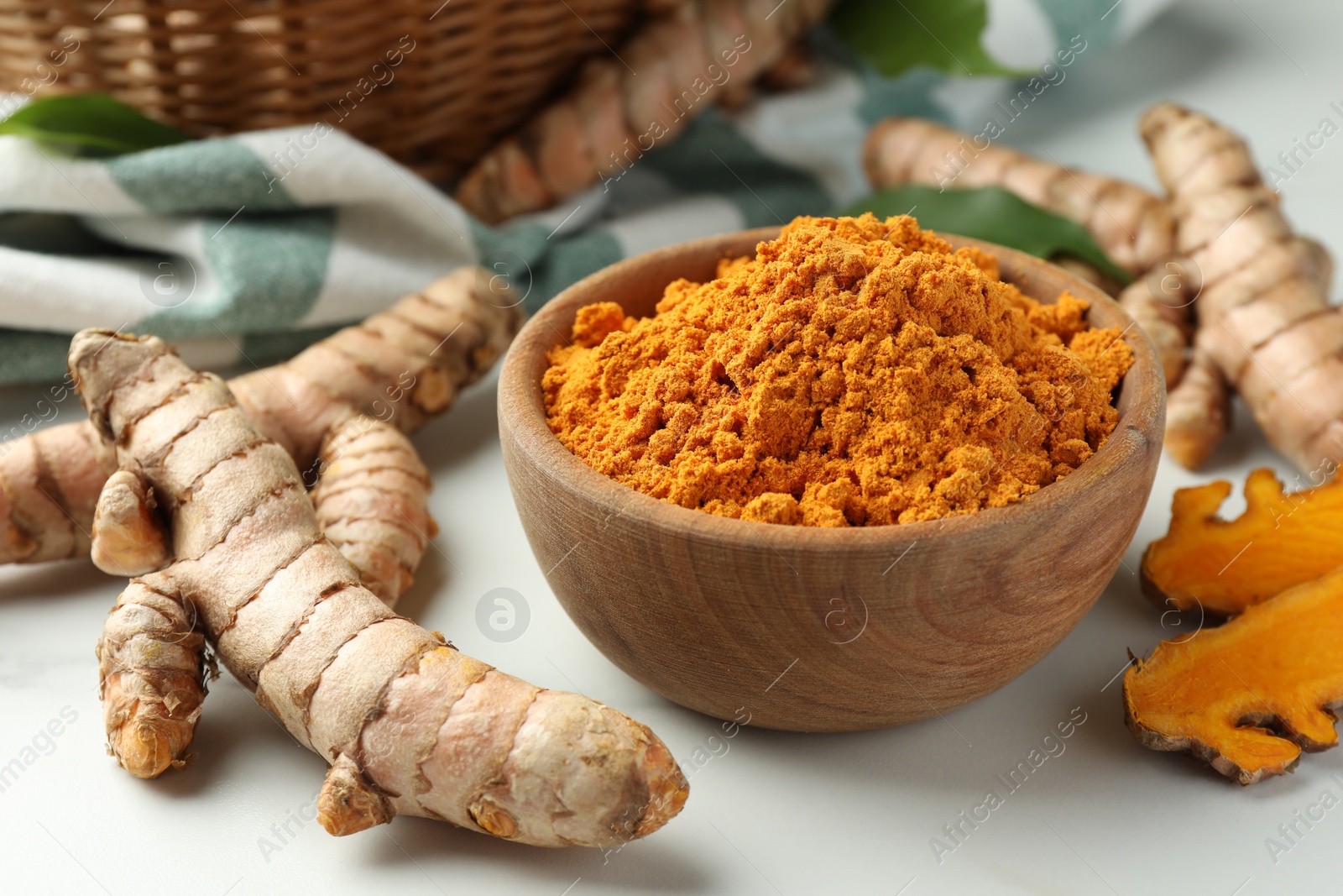 Photo of Aromatic turmeric powder and raw roots on white table, closeup