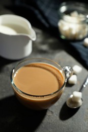 Tasty coffee with milk in cup and sugar cubes on grey table, closeup