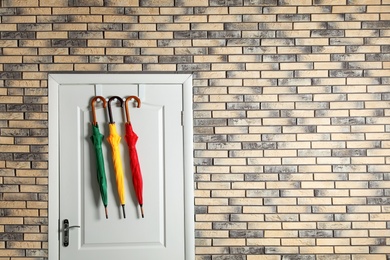 Photo of Colorful umbrellas hanging on door in brick wall with space for design