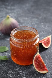 Photo of Jar with tasty sweet jam and fresh figs on black textured table