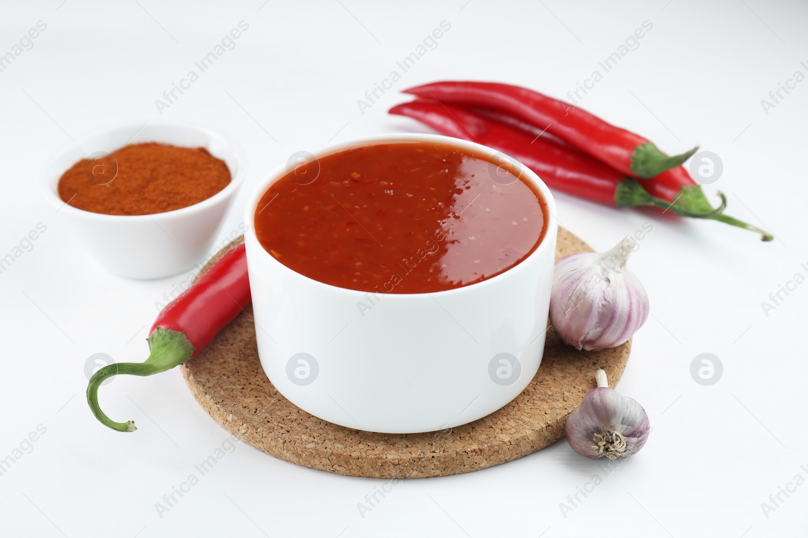 Photo of Spicy chili sauce in bowl and ingredients on white background