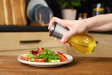 Photo of Woman spraying cooking oil onto salad on wooden table in kitchen, closeup