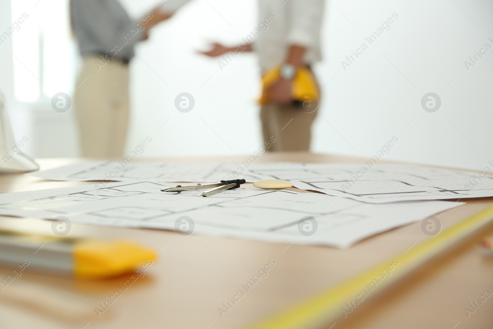 Photo of Colleagues in office, focus on table with construction drawings and tools