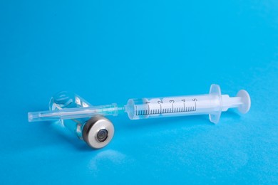 Disposable syringe with needle and vial on light blue background