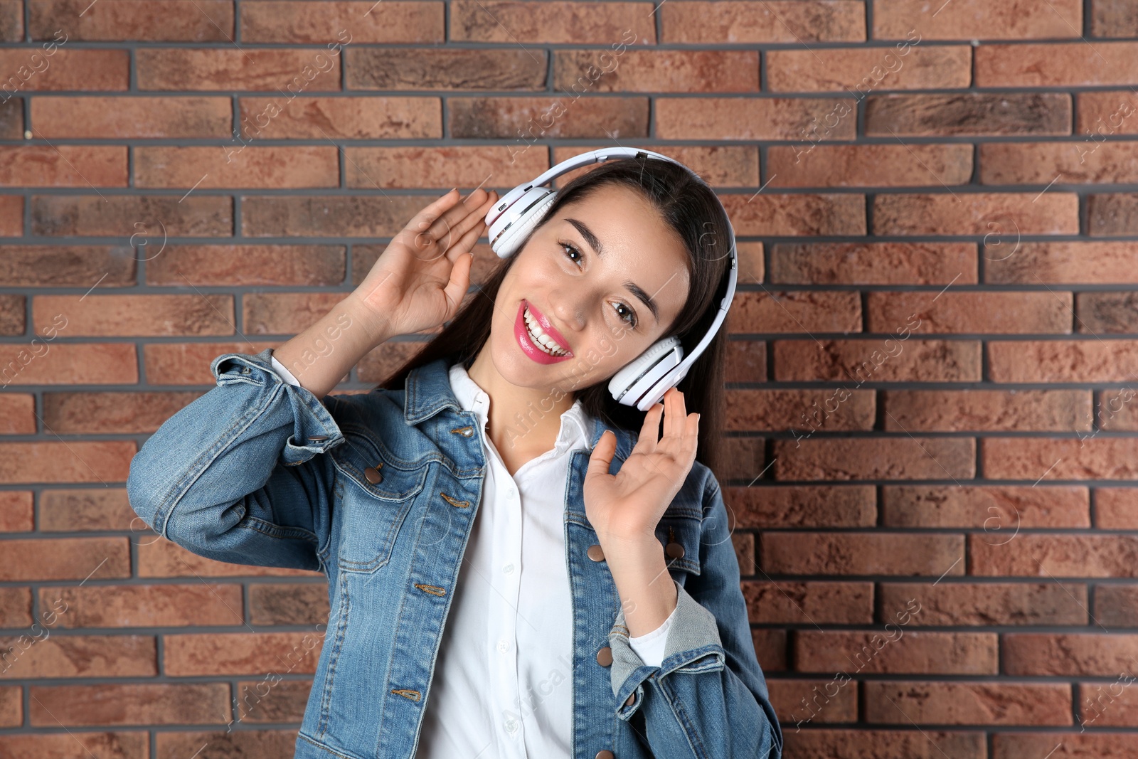Photo of Beautiful young woman listening to music with headphones against brick wall