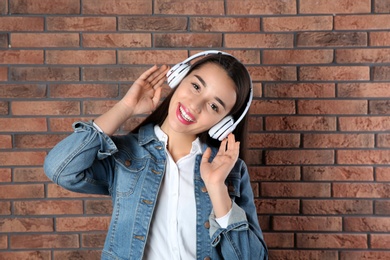 Photo of Beautiful young woman listening to music with headphones against brick wall
