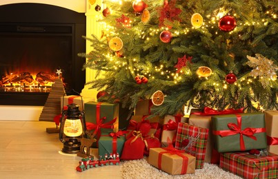 Many gift boxes, decorative elements and Christmas tree near fireplace at home