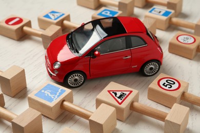 Many different miniature road signs and car on white wooden table, closeup. Driving school