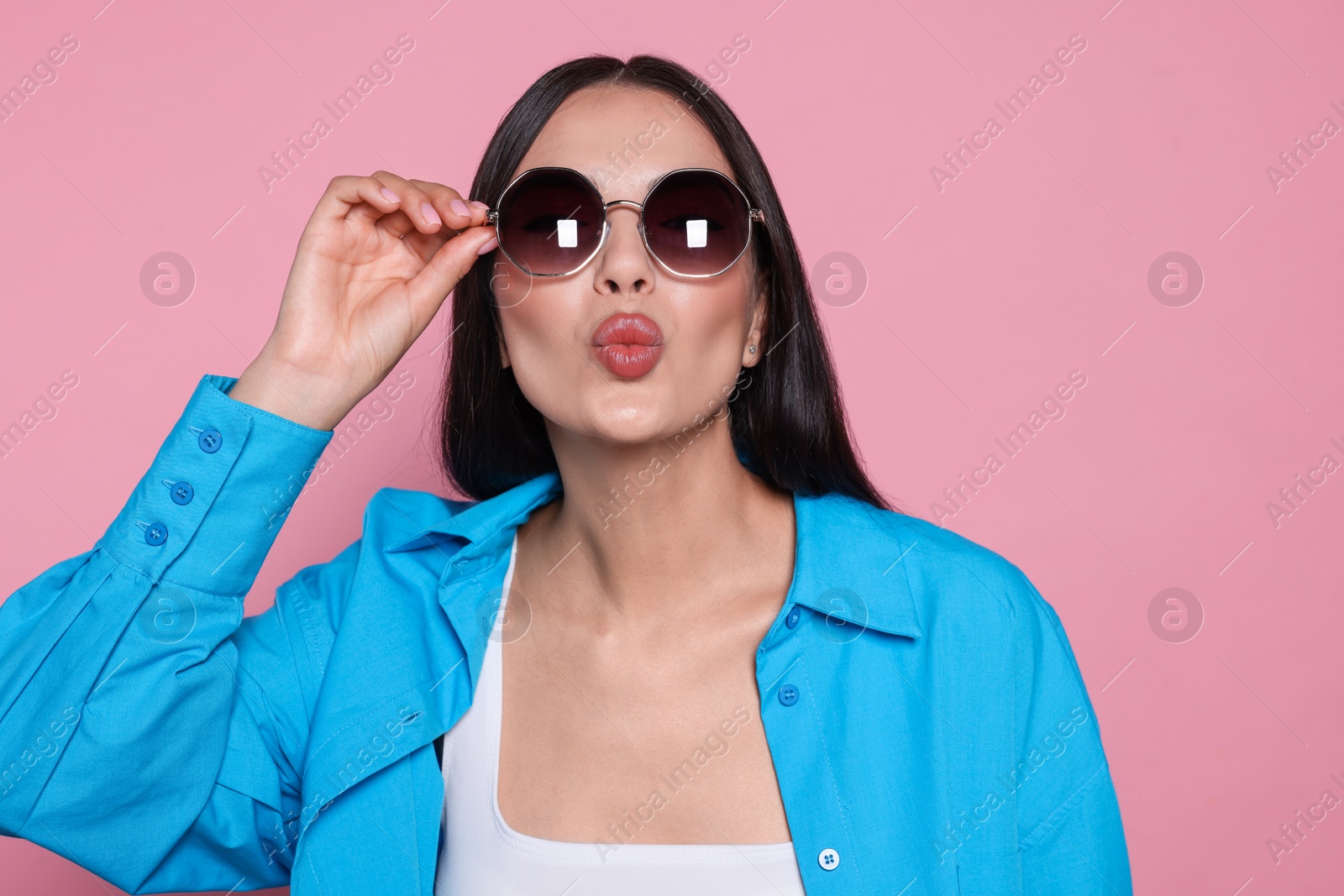 Photo of Attractive happy woman touching fashionable sunglasses against pink background. Space for text