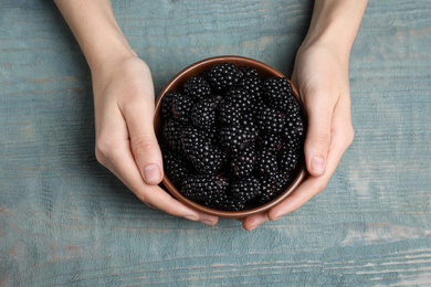 Photo of Woman with bowl of blackberries at blue wooden table, top view