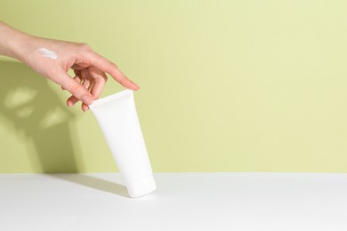 Woman with tube of cream on color background, closeup. Space for text