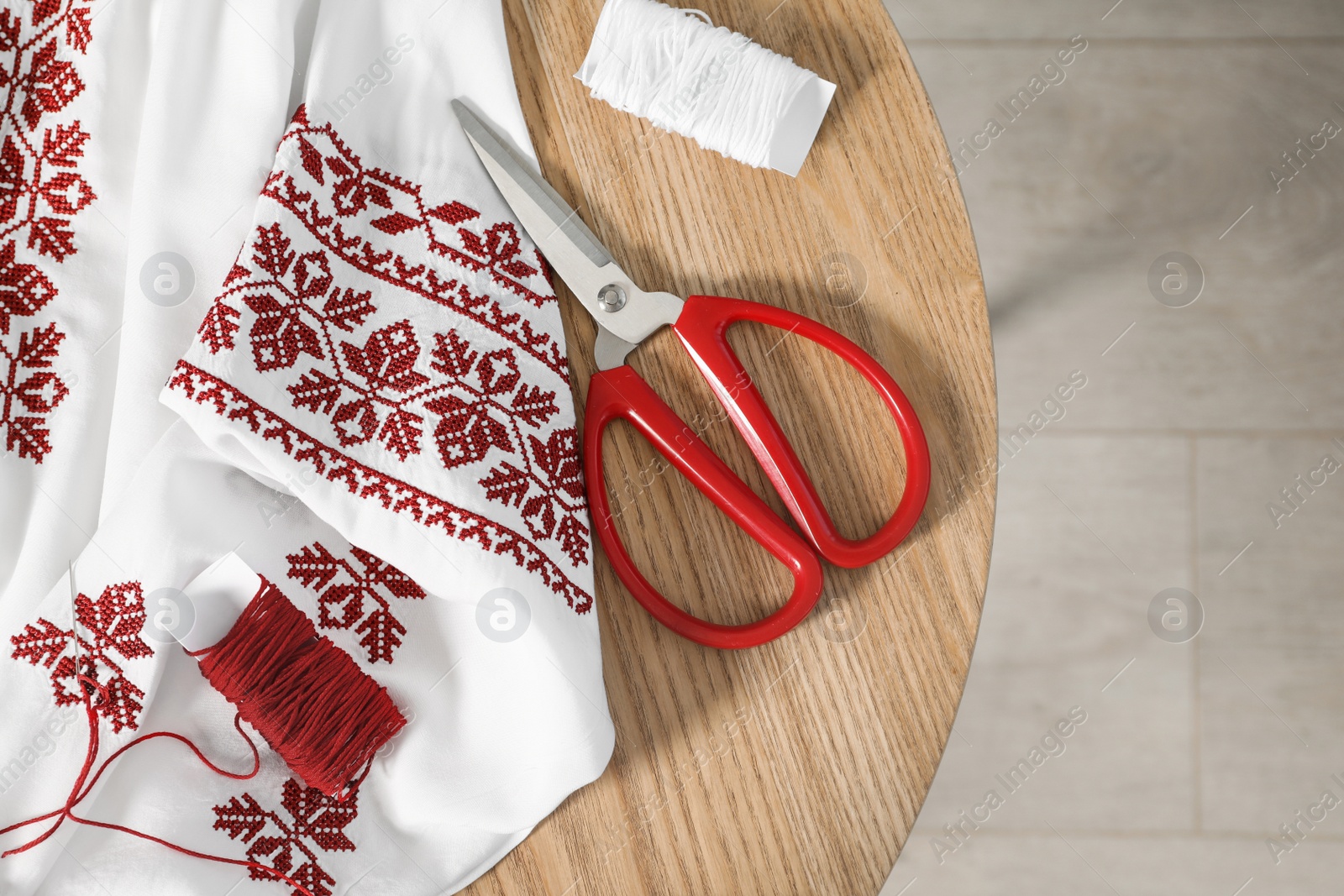 Photo of White shirt with beautiful embroidery design, threads and scissors on wooden table, flat lay. Ukrainian national clothes