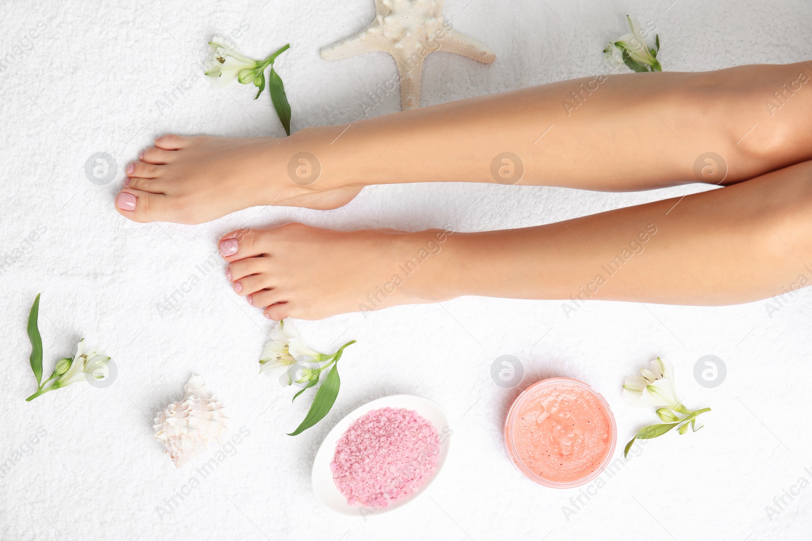 Photo of Woman with beautiful legs, cosmetic and flowers on white towel, top view. Spa treatment