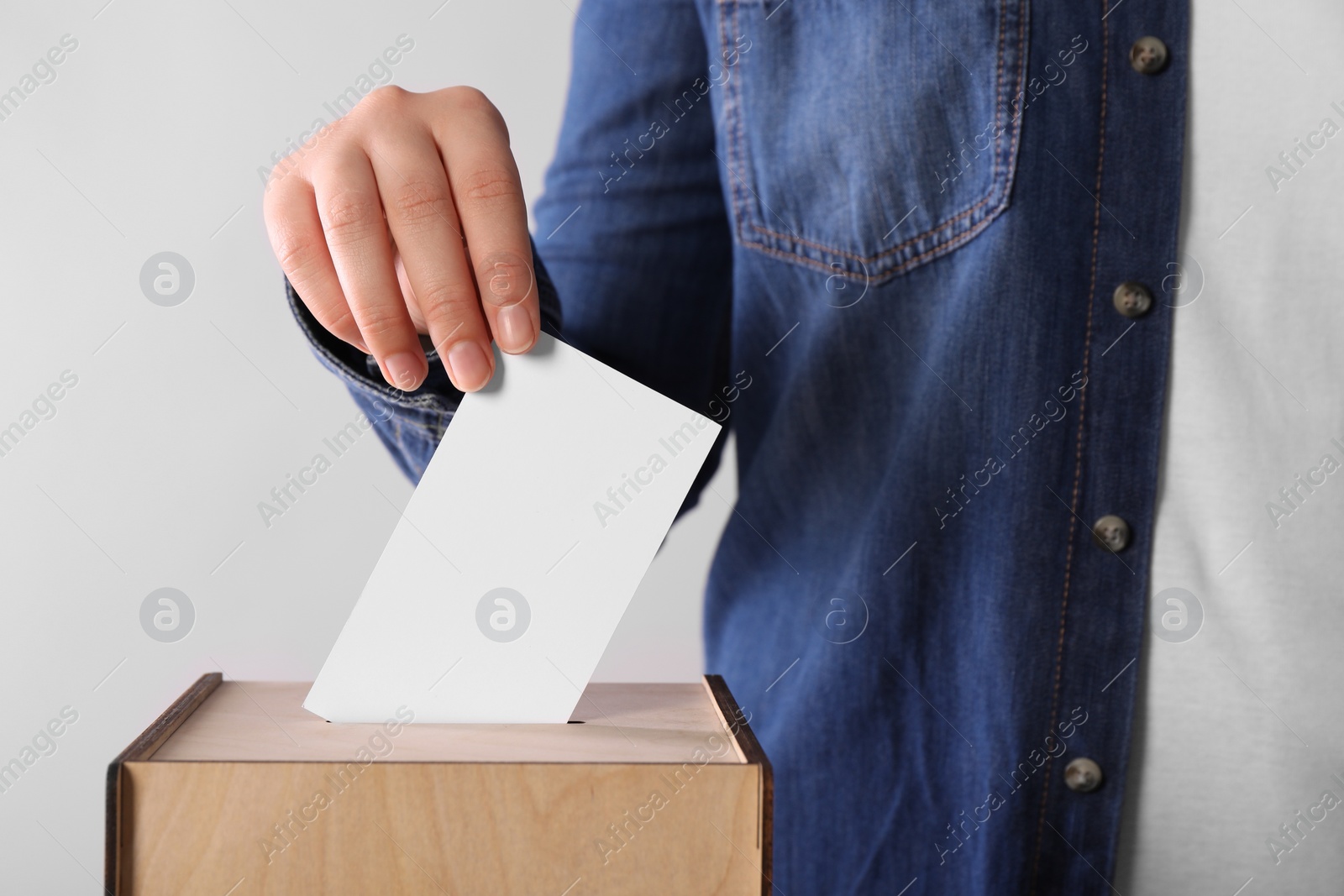 Photo of Woman putting her vote into ballot box on light grey background, closeup