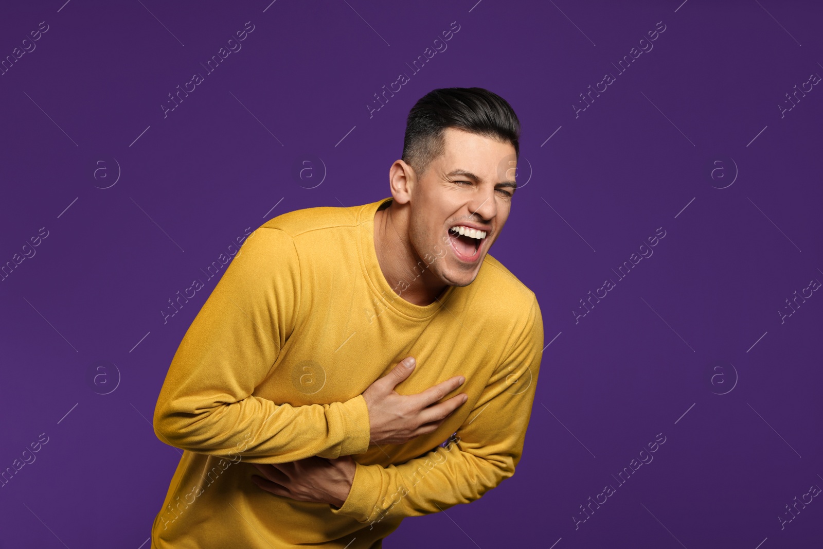 Photo of Handsome man laughing on purple background. Funny joke