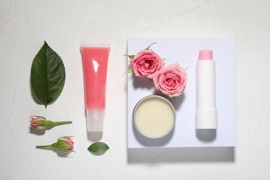 Photo of Flat lay composition with lip balms and rose flowers on white textured background