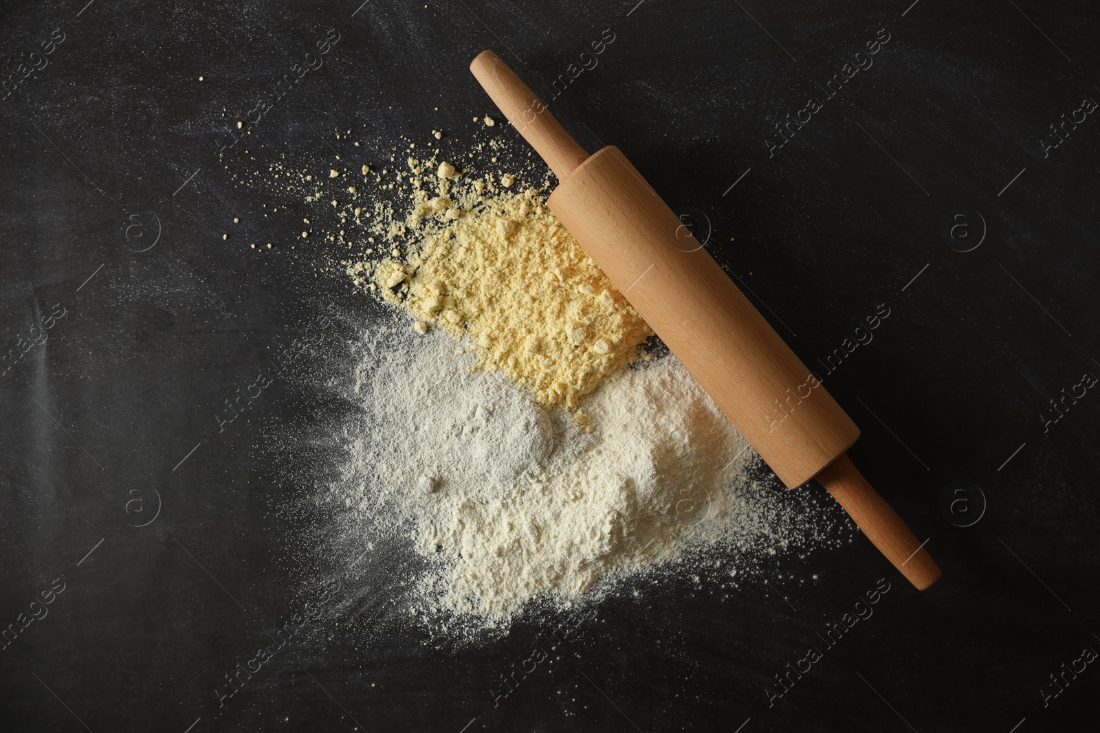 Photo of Rolling pin and different types of flour on black table, top view